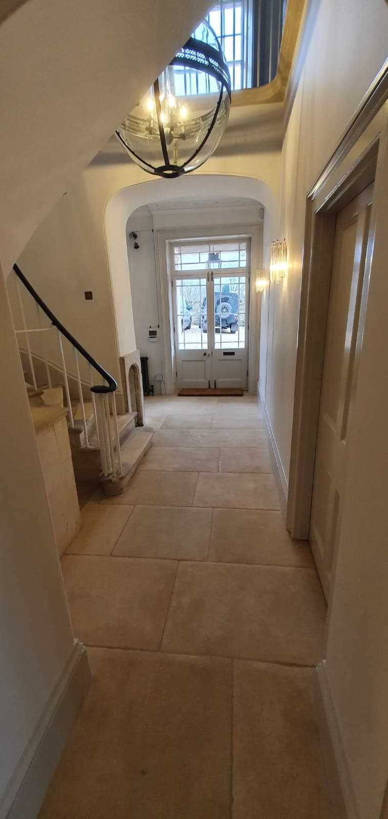 Hallway after a house renovation, with stone floor flags, a stone staircase and a lantern pendant light leading to glazed front doors