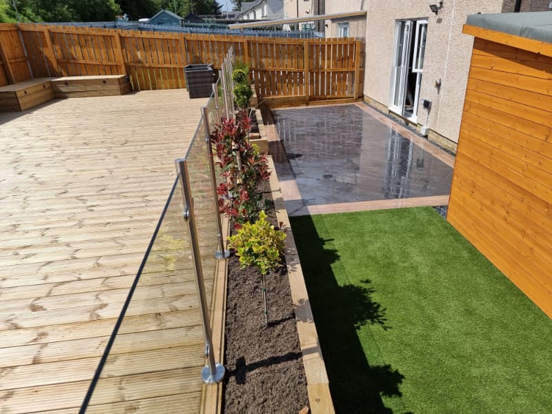 A finished garden with decking, a paved patio, fencing and raised planting