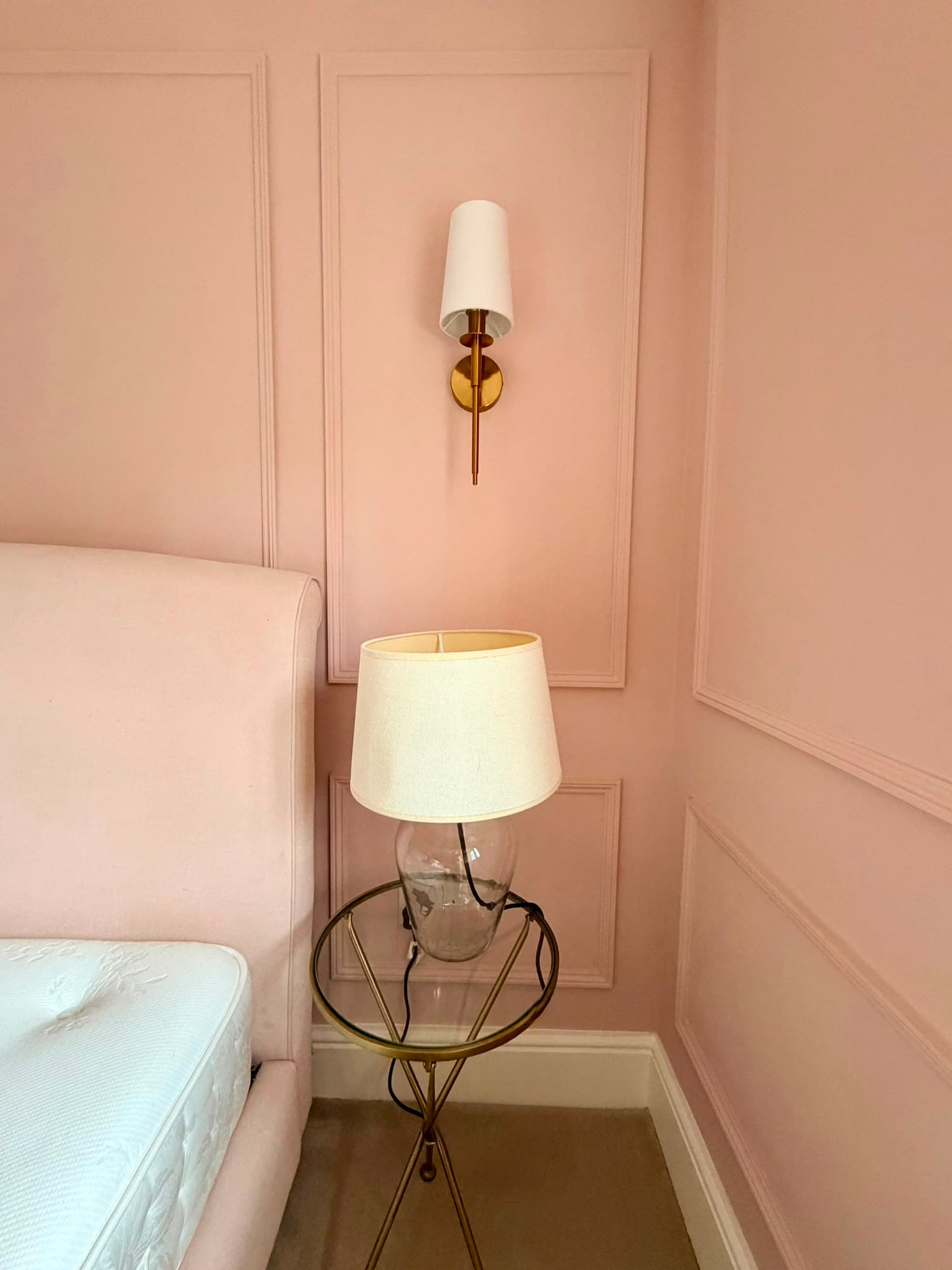 Soft pink painting and decorating finish on bedroom wall panelling beside the bed and a brass wall light